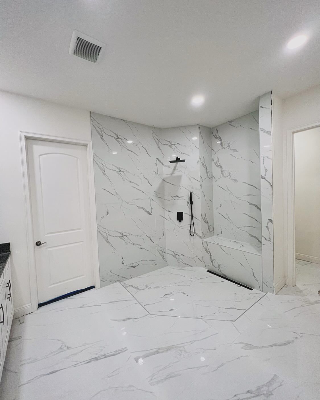 Modern white bathroom with marble tile walls, walk-in shower, and white door.