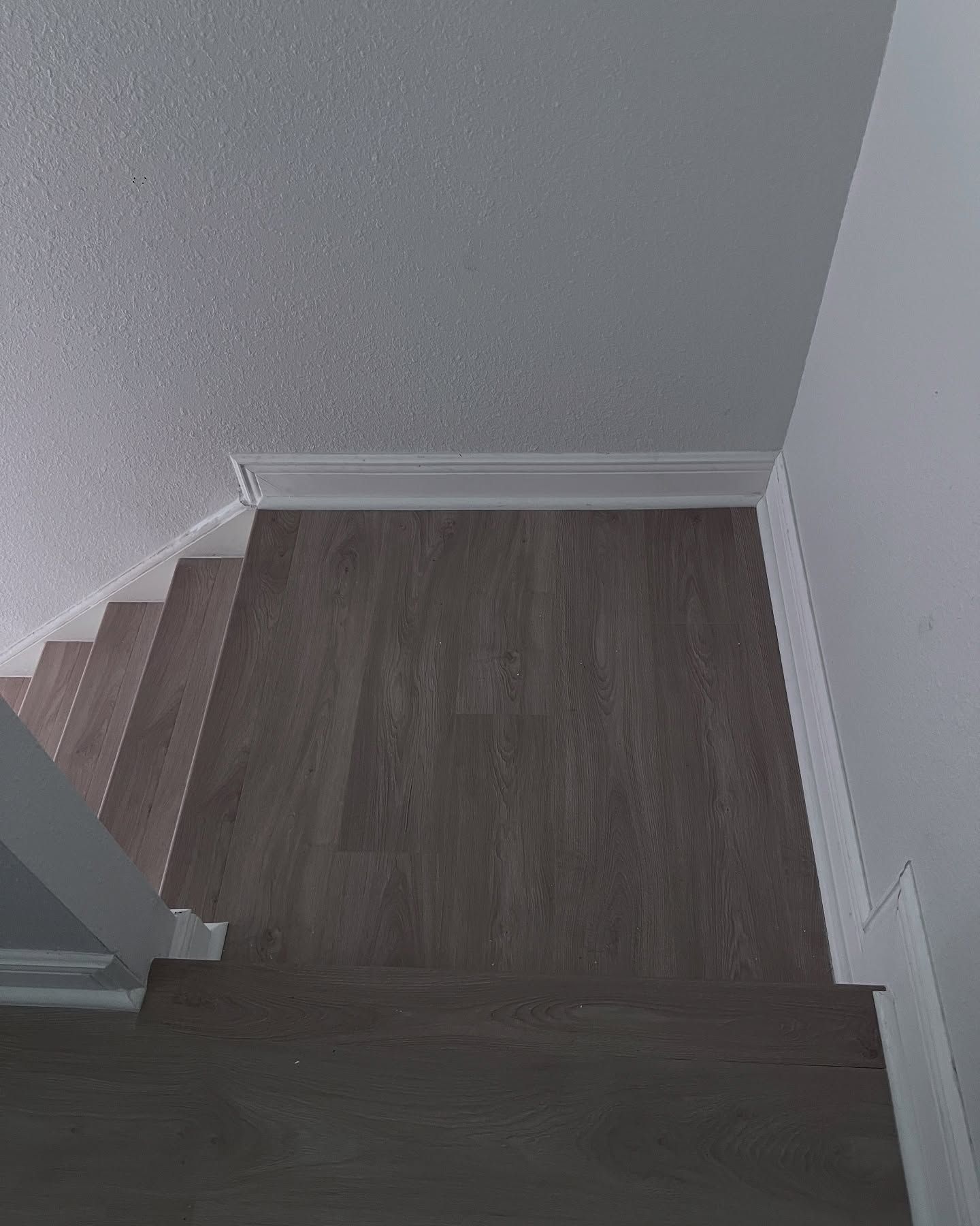 Top of a staircase with dark wood flooring, white walls, and light-colored steps visible on the left.