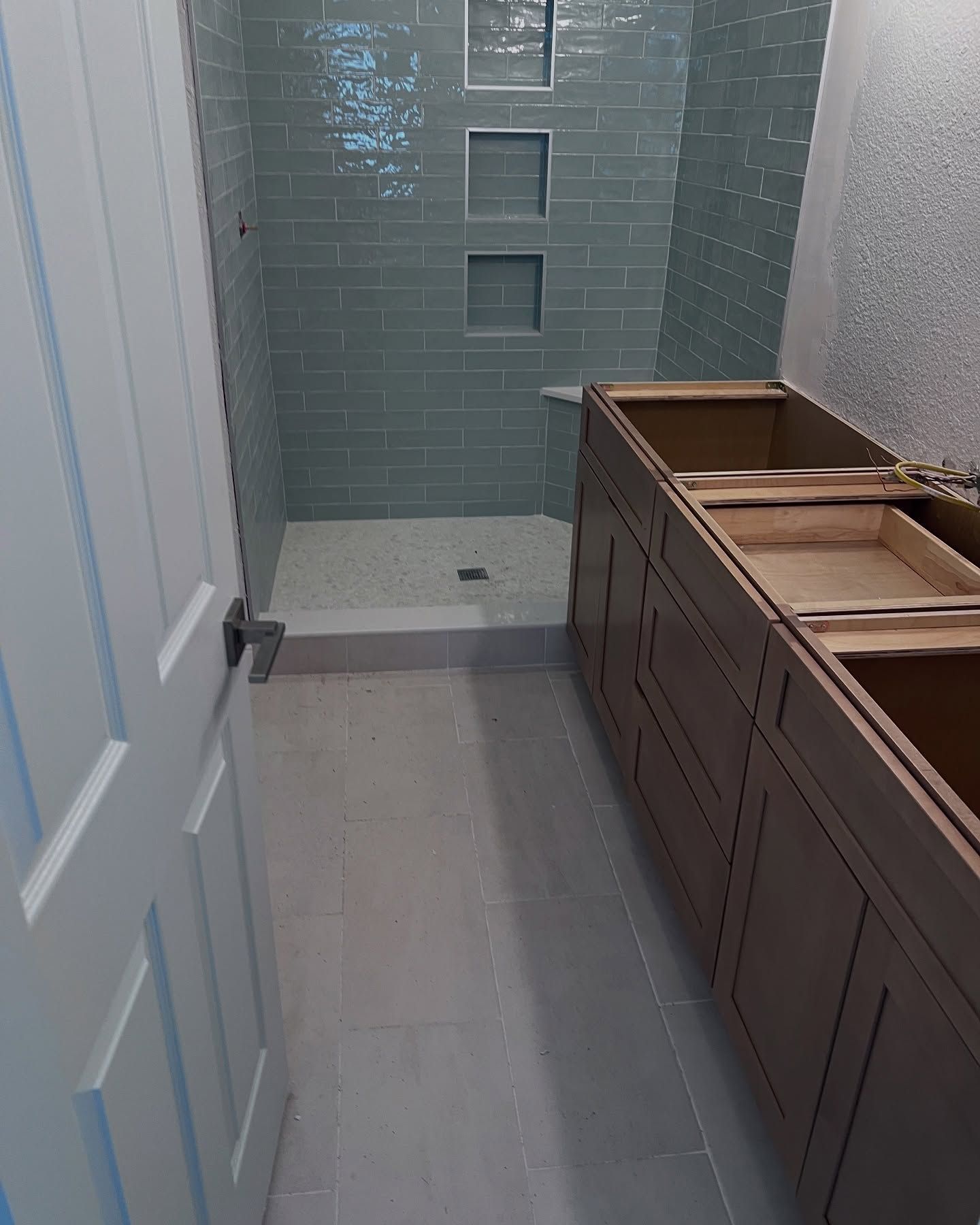 Modern bathroom with blue tile shower, gray floor, and wood vanity under construction