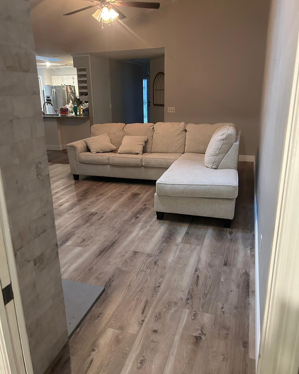 Empty living room with beige sectional sofa and wood-look flooring, viewed from a doorway