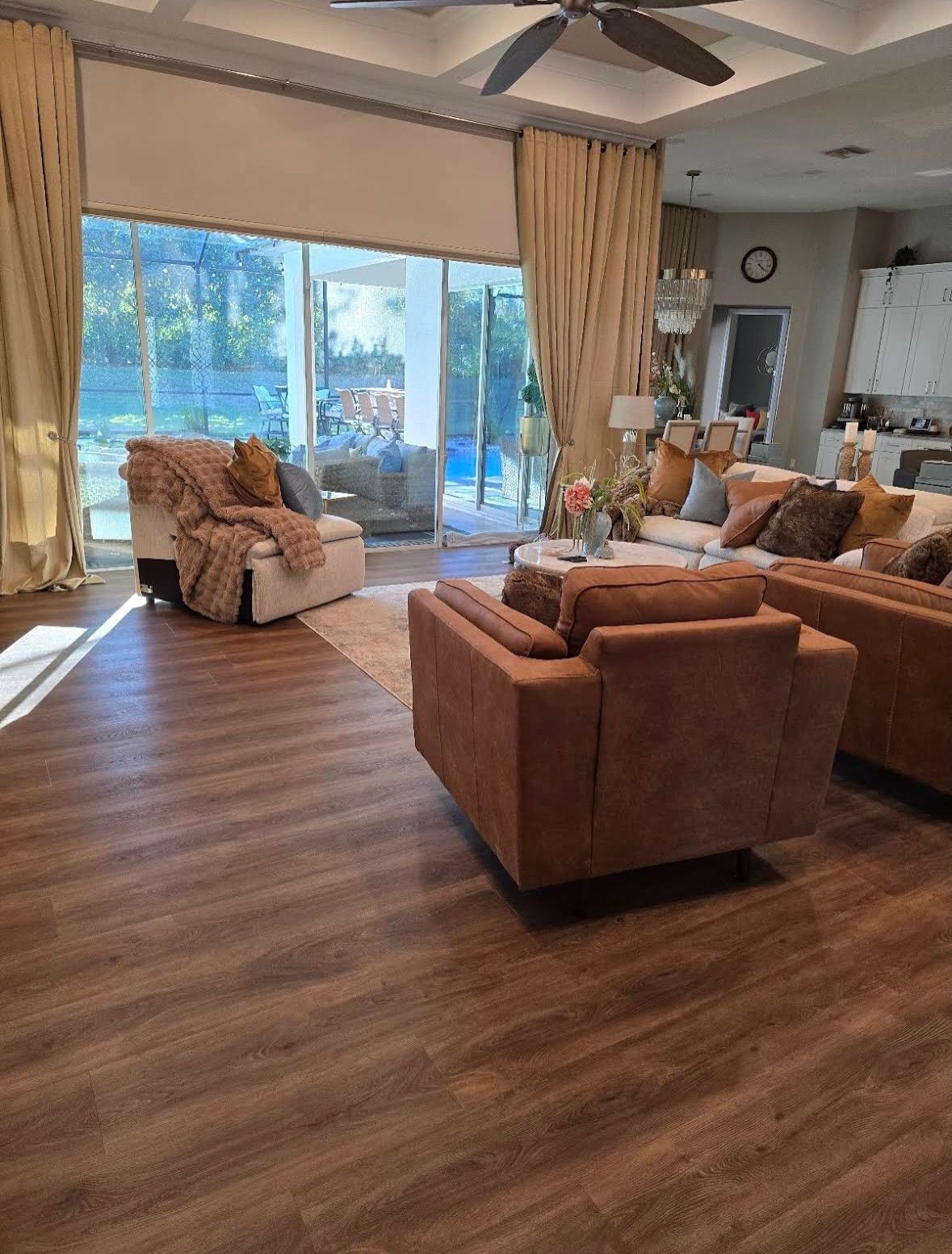 Sunlit living room with brown sofas, wood floor, and large sliding glass doors.