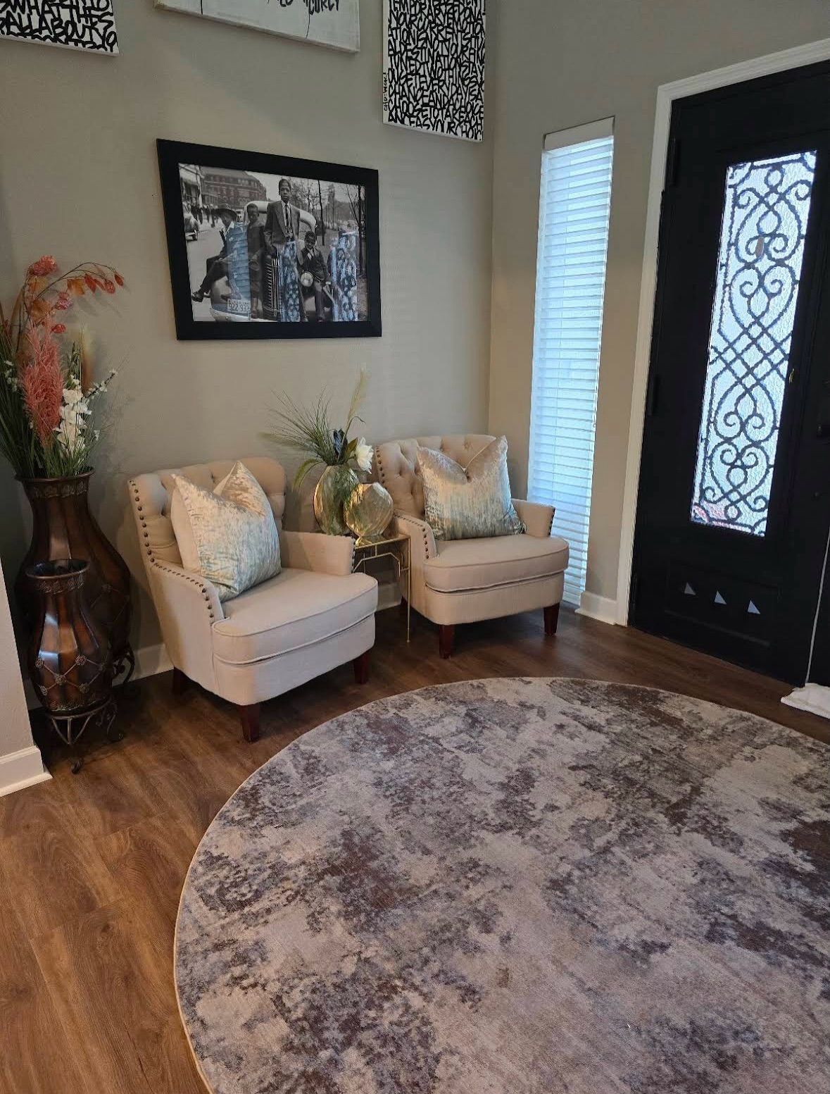 Cozy entryway with two cream chairs, round rug, framed art, and a black front door.