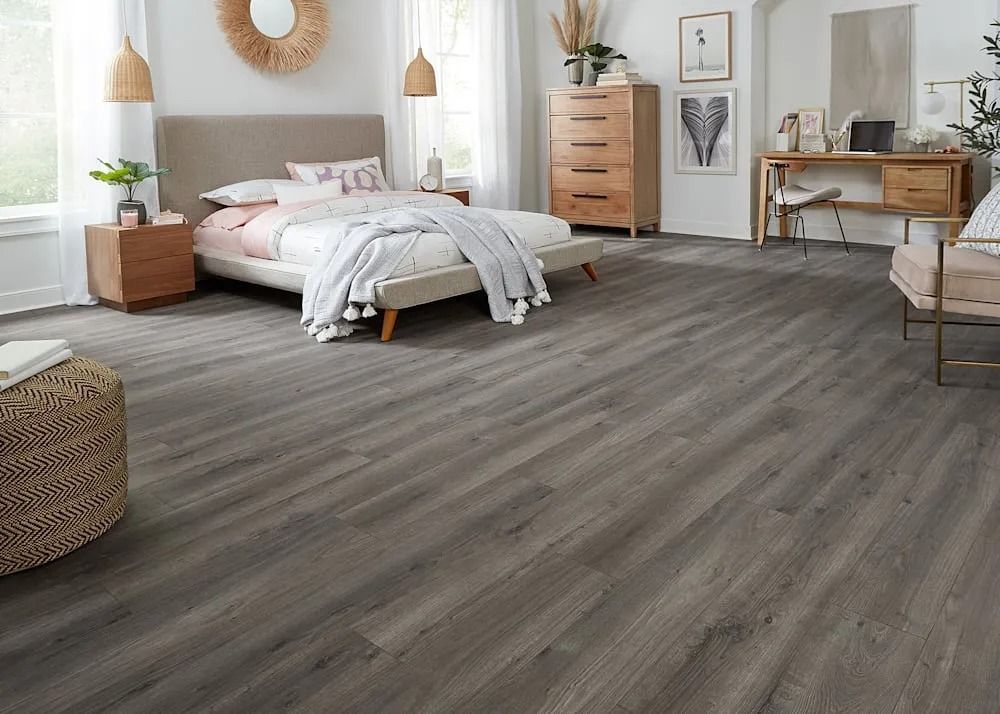 Bright modern bedroom with gray wood flooring, a bed, wooden dresser, desk, and woven accents