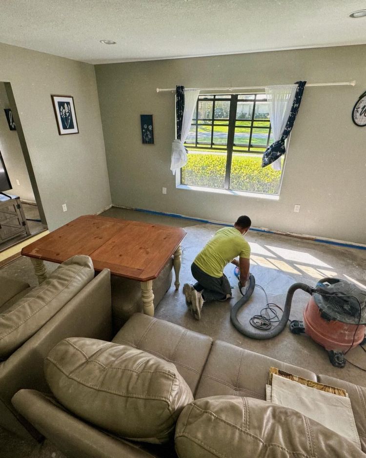 Person vacuuming in a living room with sofa, table, and window covered in protective plastic.