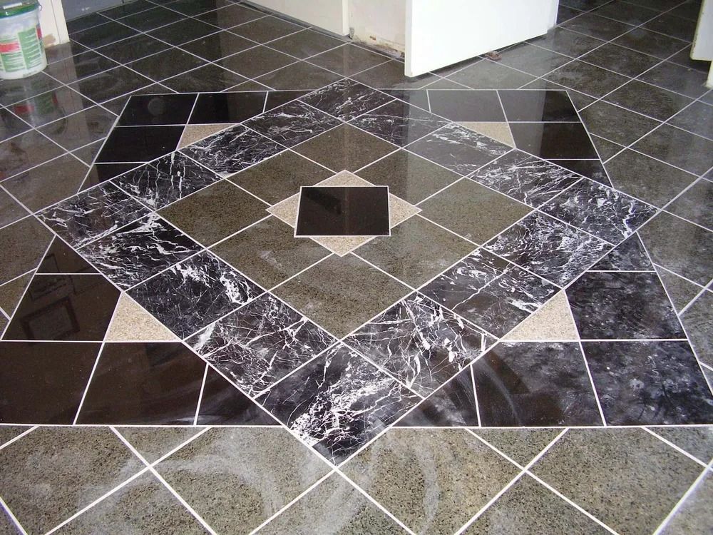 Patterned tiled floor with a diamond design in black, gray, and beige, centered by a small square tile.