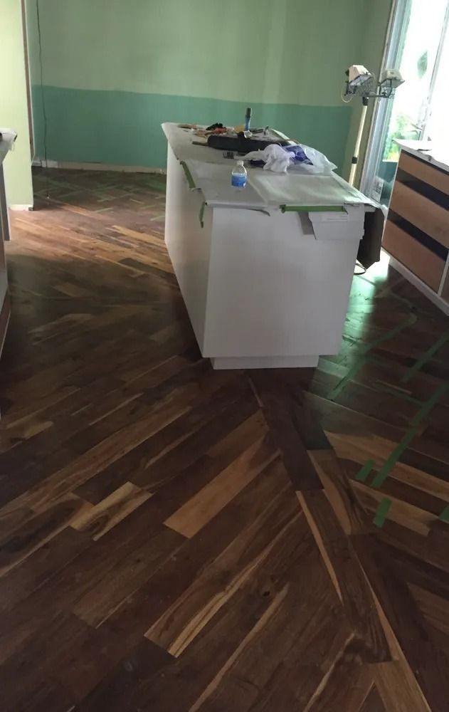 Empty room with dark wood floors and a white island table near a green wall and window.