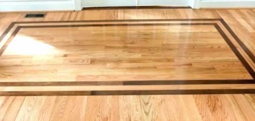 Wooden floor with a rectangular dark border inlay, lit by sunlight from a nearby window.