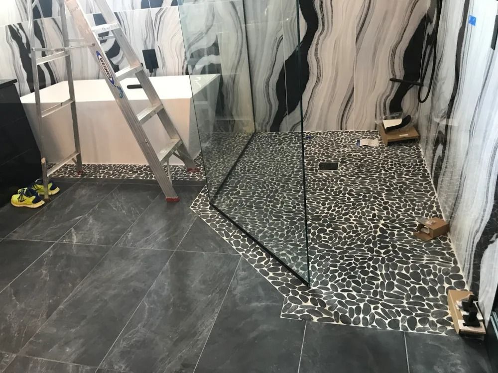 Bathroom under renovation with a ladder, sink vanity, and tiled shower area with tools on the floor