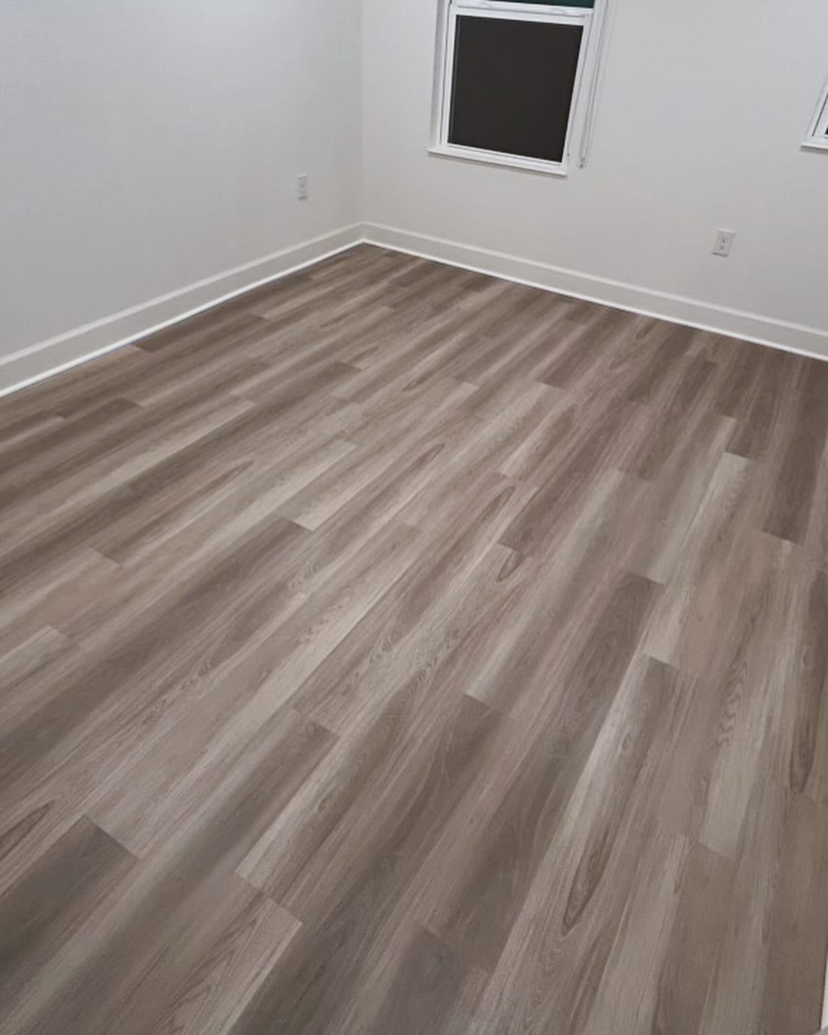 Empty room with gray wood-look flooring, white walls, and a window.