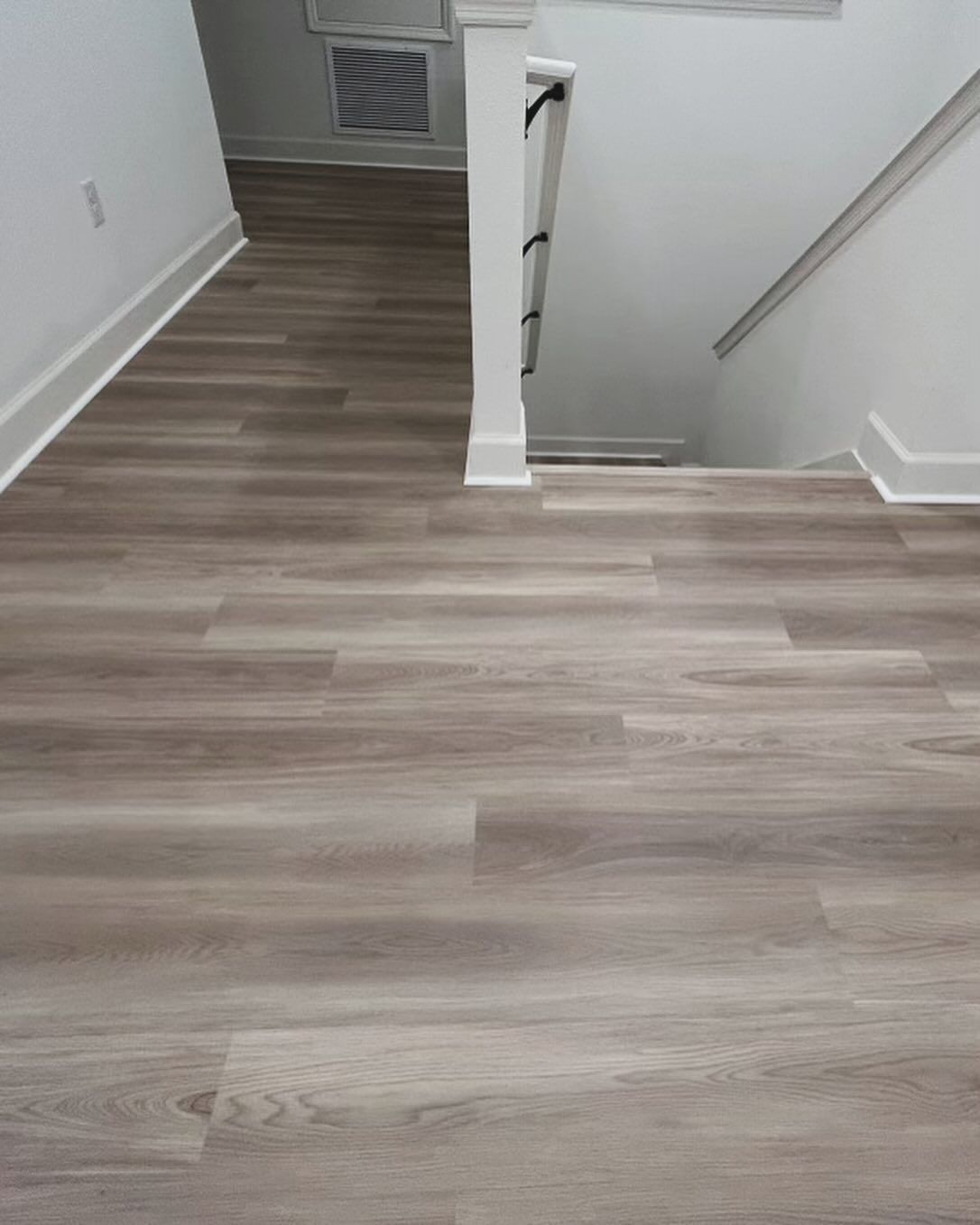 Hallway with gray wood flooring and white walls, opening to a stairwell on the right