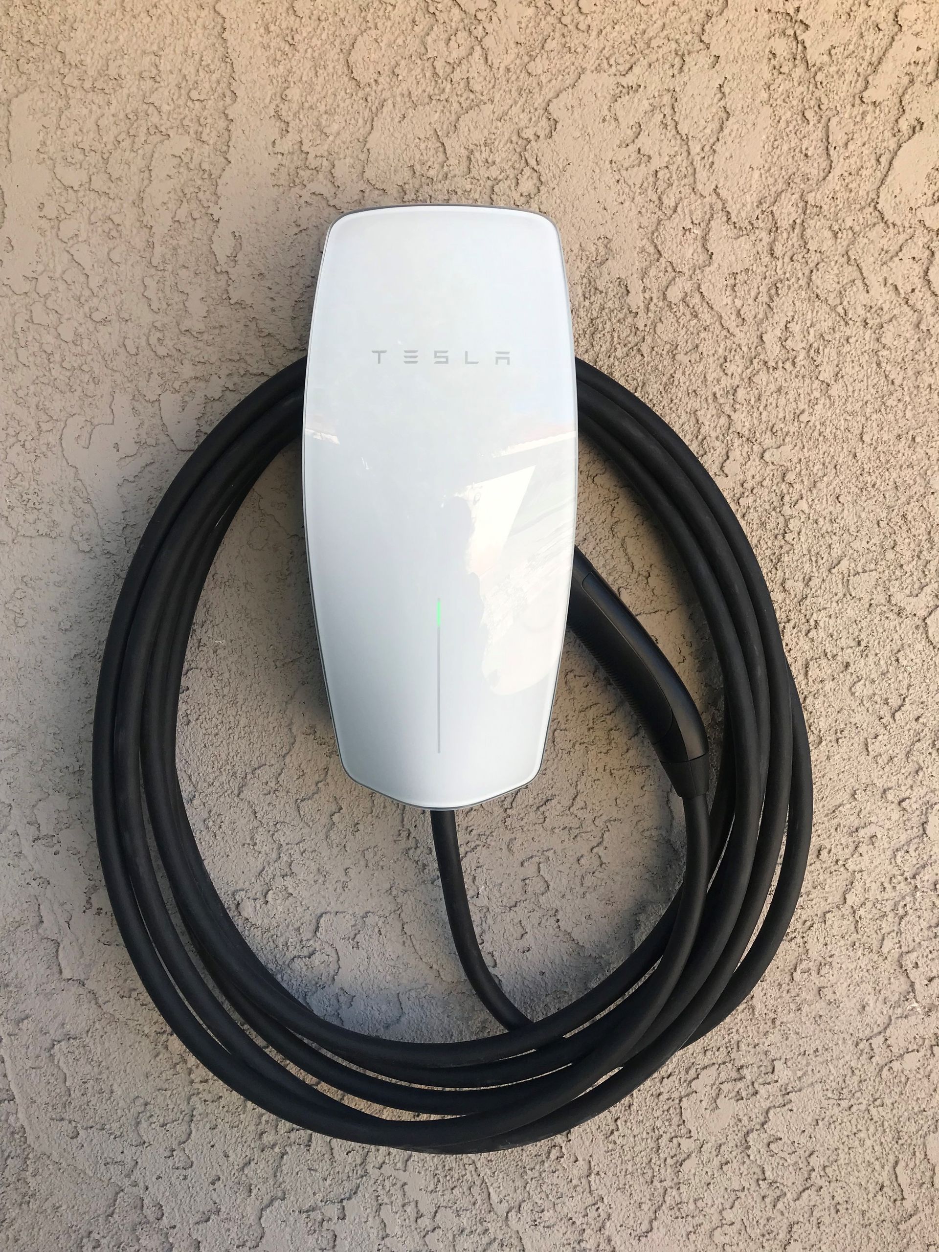 A white tesla charging station with a black cable attached to it