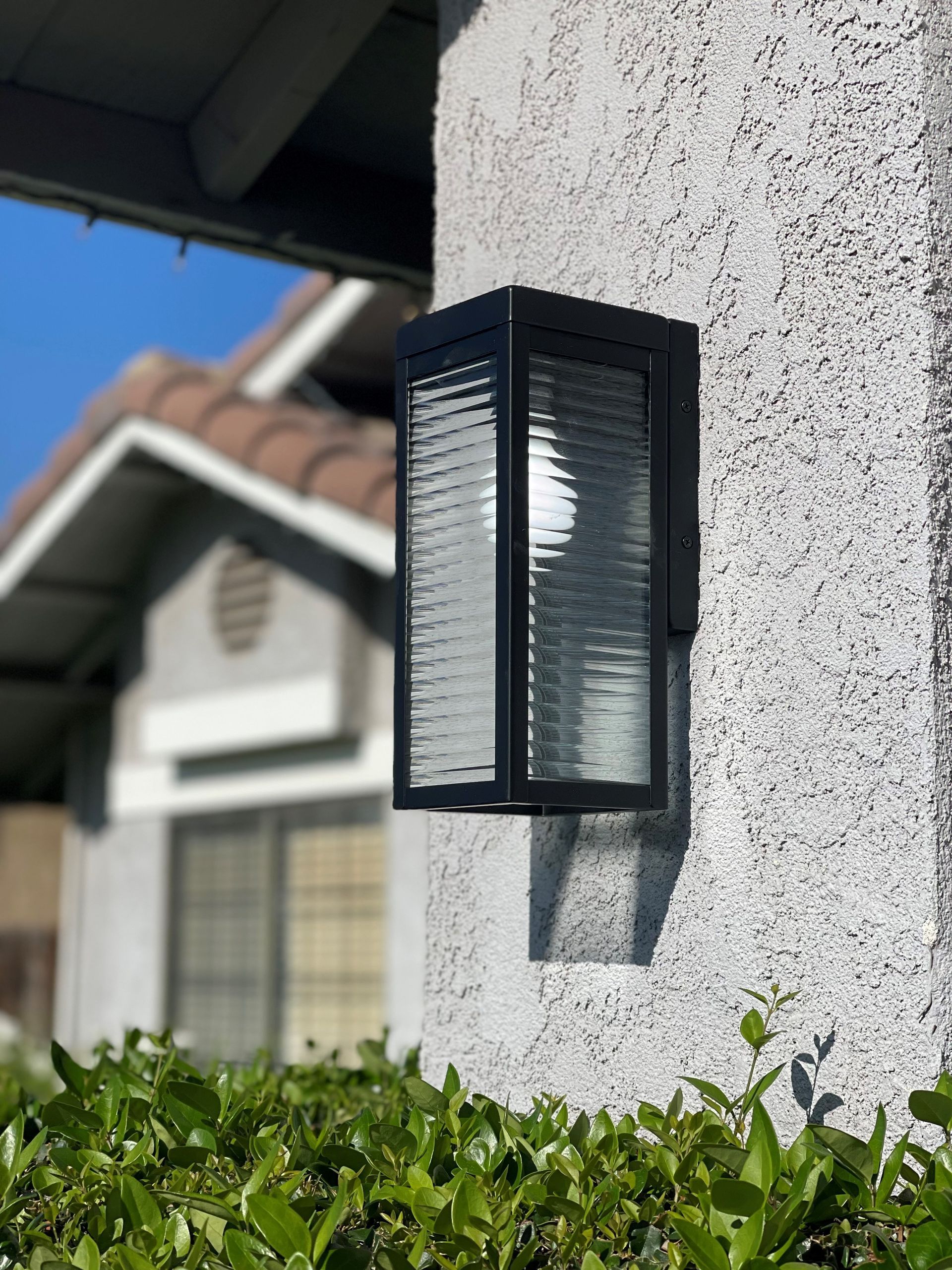 A black wall light is on the side of a house.