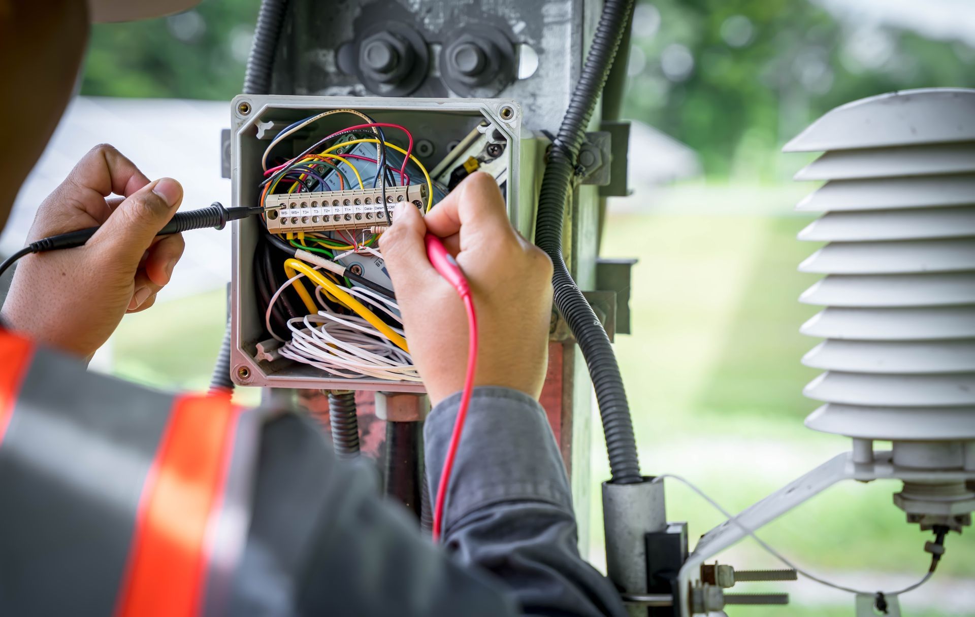 A man is working on an electrical box with a voltmeter.