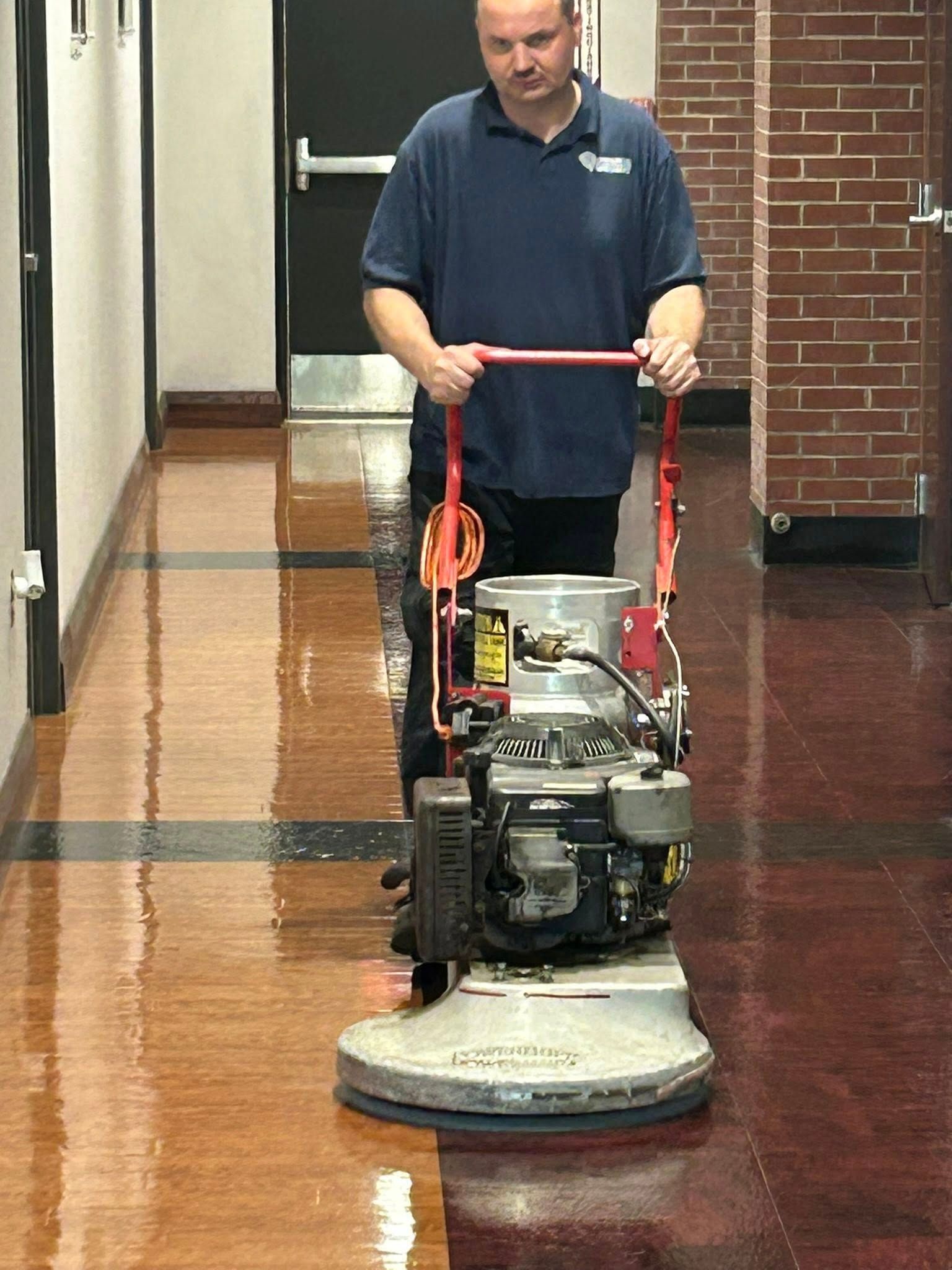 A person uses a floor buffer in a hallway with shiny, wooden flooring.