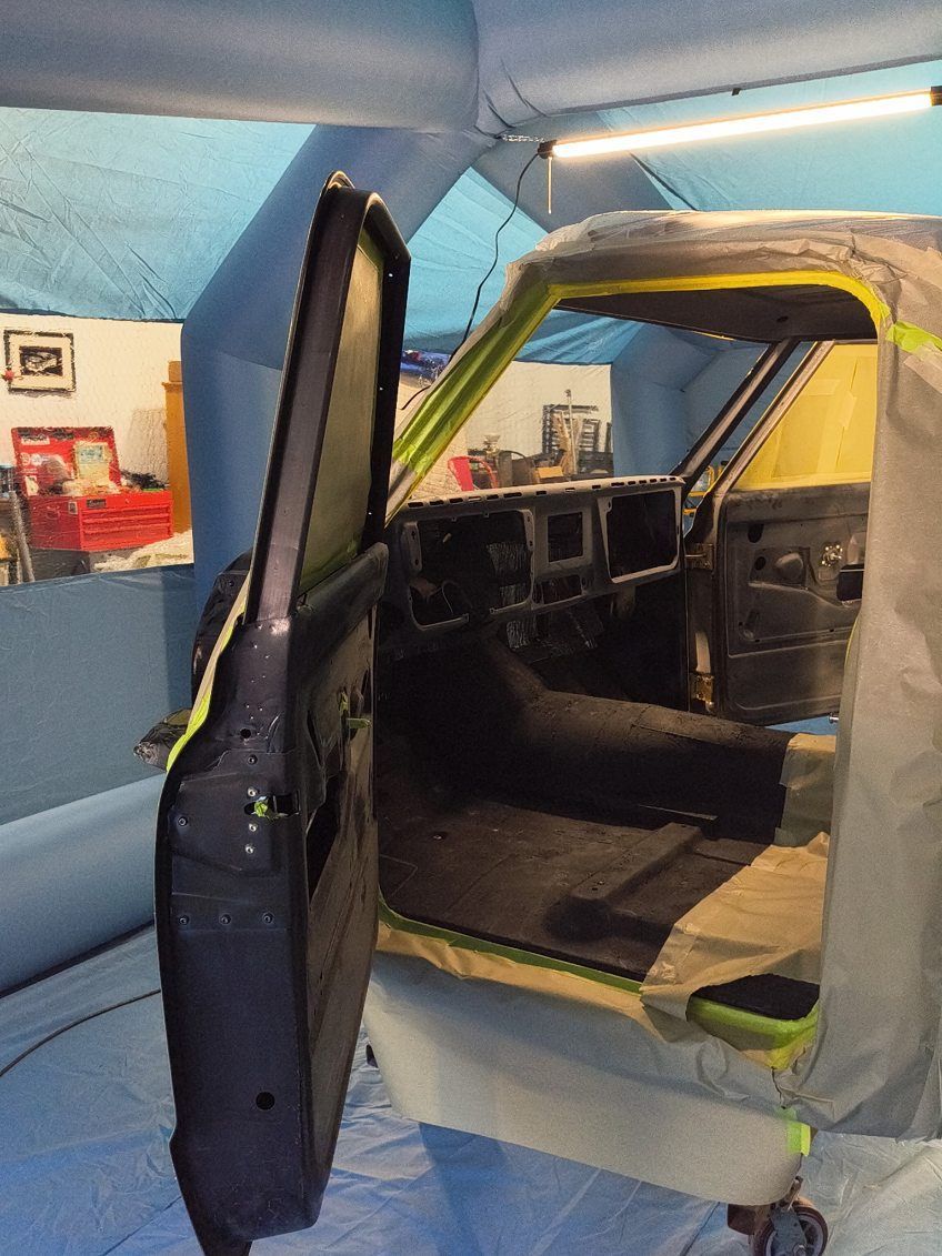 Exposed car interior with open door in a workshop, showing stripped dashboard and seats.