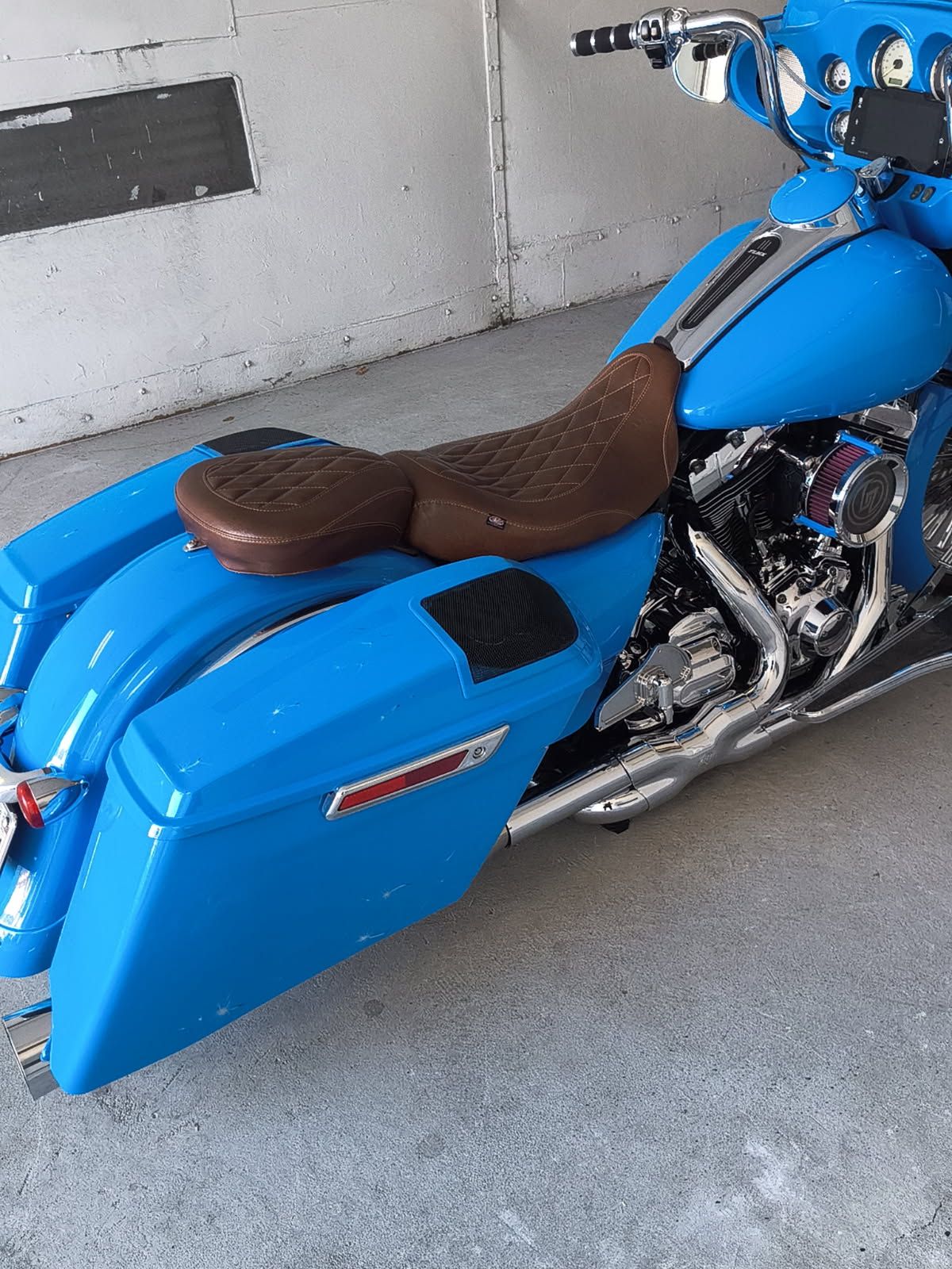 Blue custom motorcycle with brown seat and matching saddlebags parked in a garage
