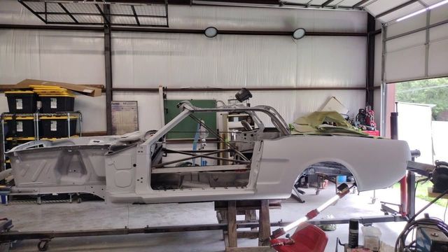 Partially assembled white car body in a workshop garage, with exposed frame and tools around it