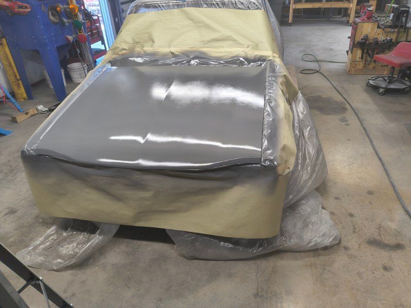 Car body in a workshop, partially sanded and masked with plastic sheeting and tape