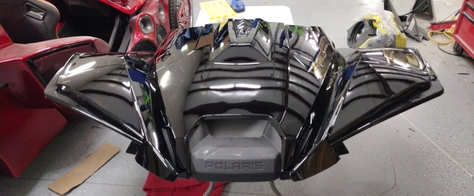 Glossy black snowmobile hood with vents, shown indoors on a showroom floor