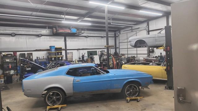 Blue-and-silver classic car in a garage with a yellow car in the background