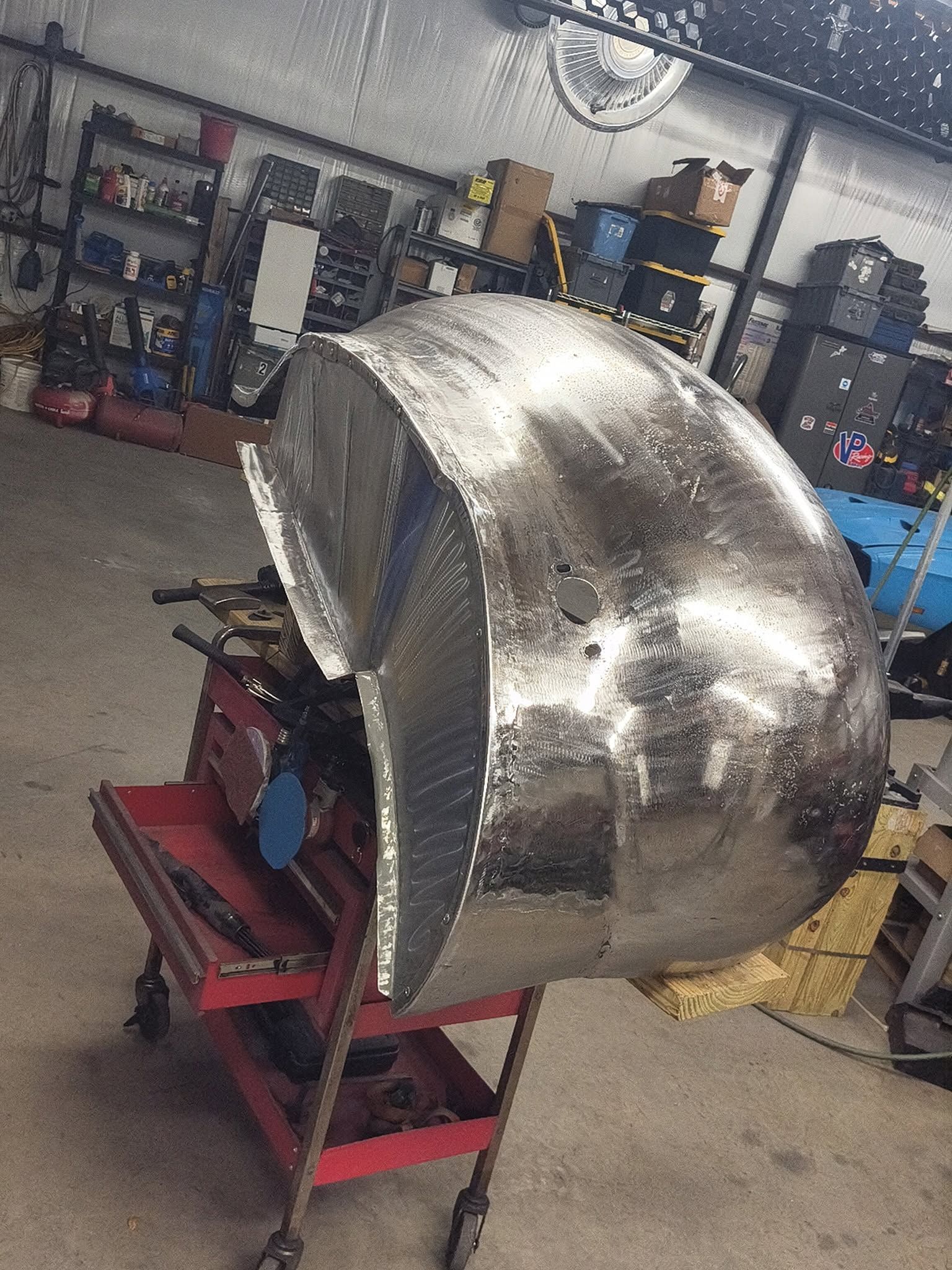 Shiny metal car body shell on a red stand in a workshop garage