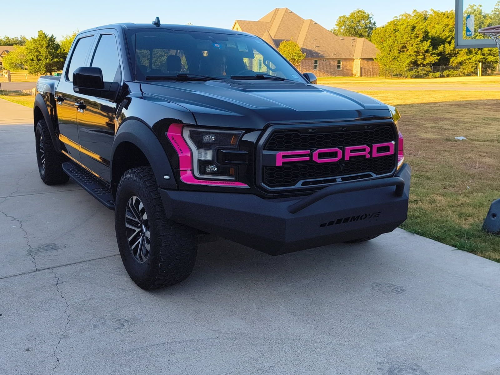 Black Ford pickup with pink grille accents parked on a suburban driveway