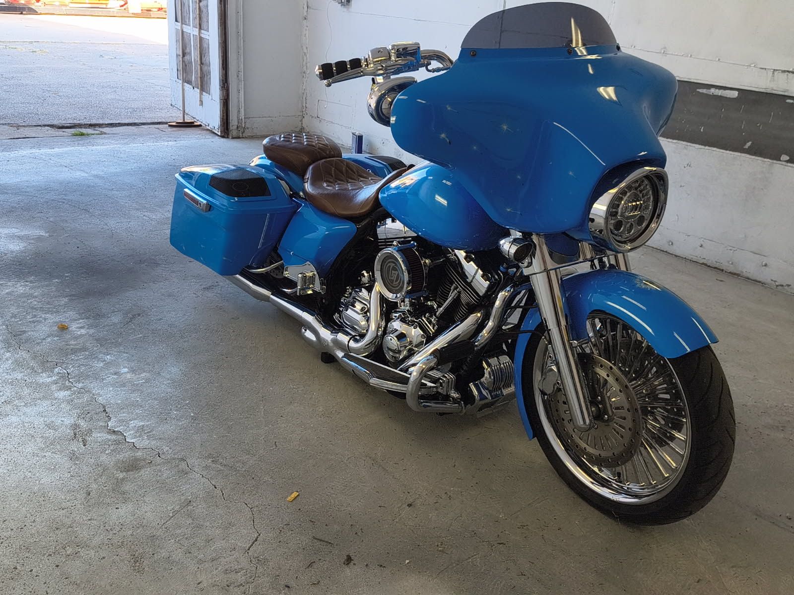 Blue touring motorcycle parked indoors on a concrete floor near an open garage door.