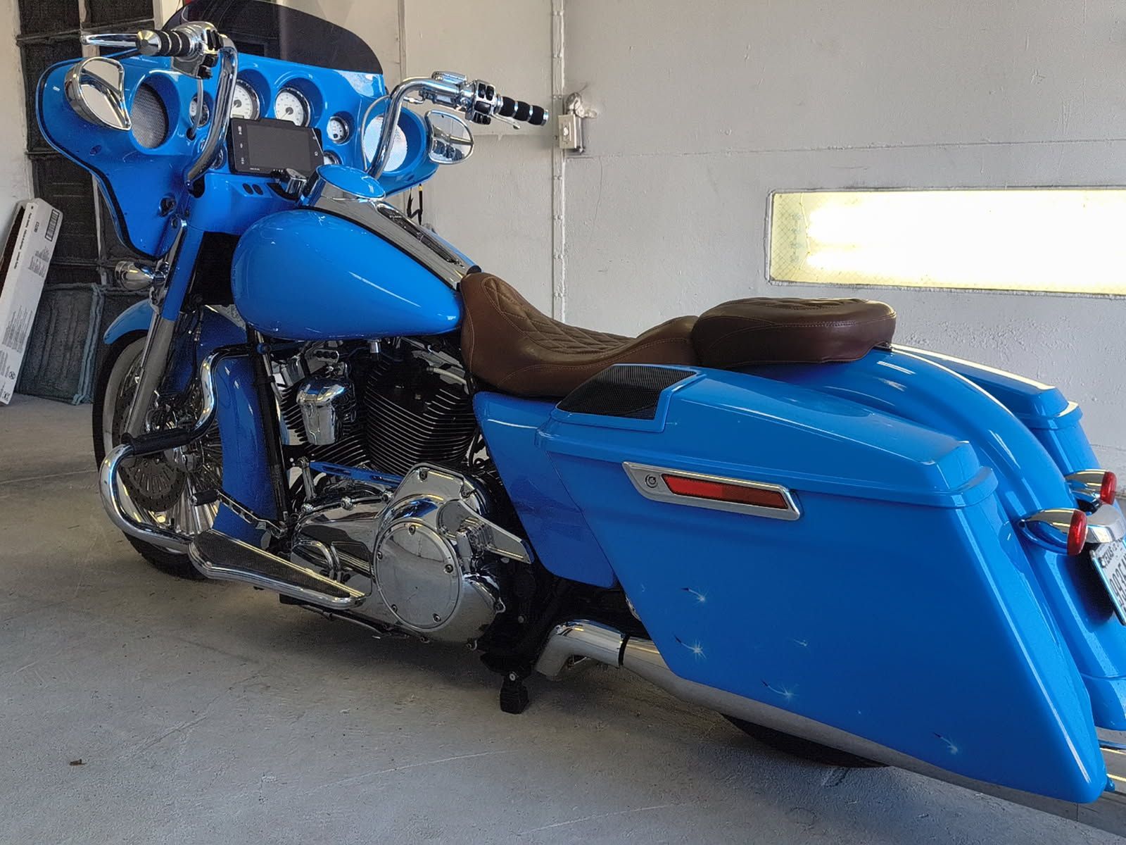 Blue touring motorcycle parked indoors on a concrete floor, side view with saddlebags and brown seat