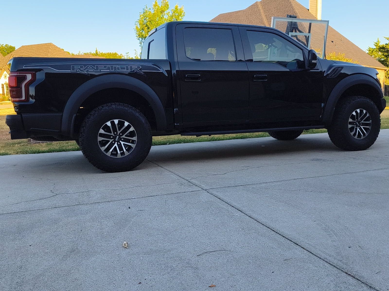 Black pickup truck parked in a driveway beside a house, side view.