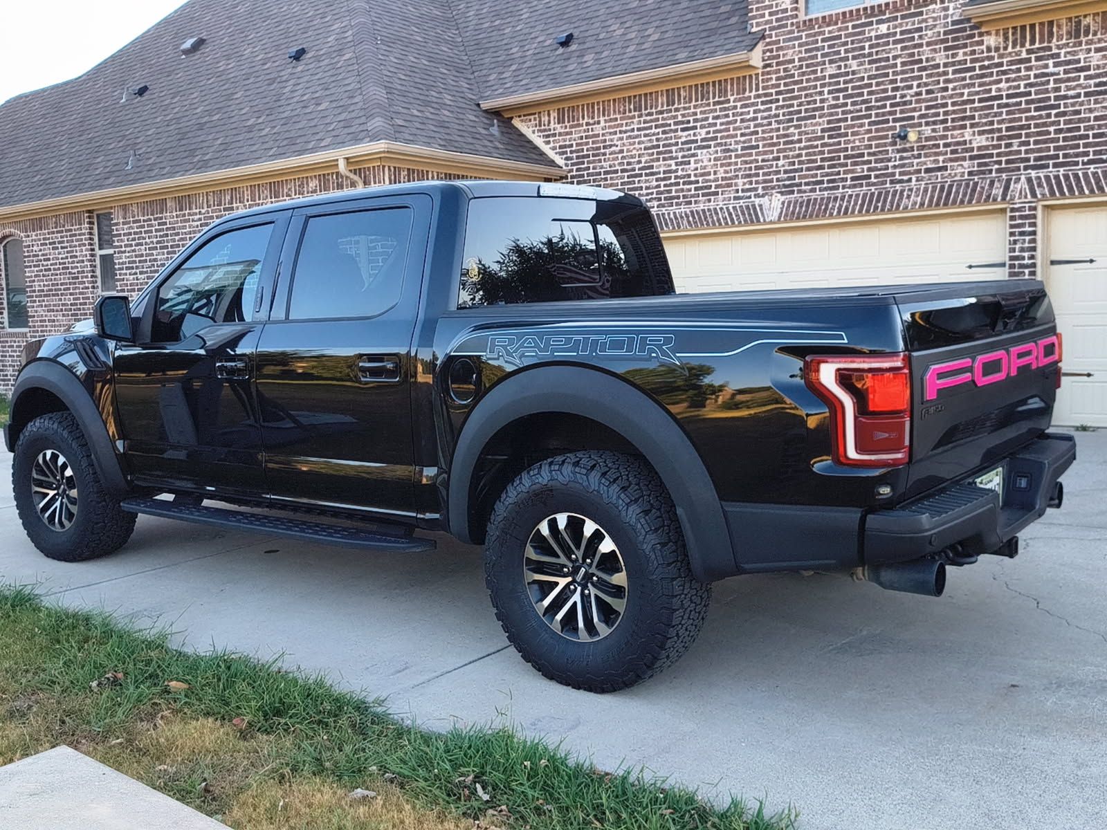 Black Ford pickup truck parked in a driveway beside a brick house.