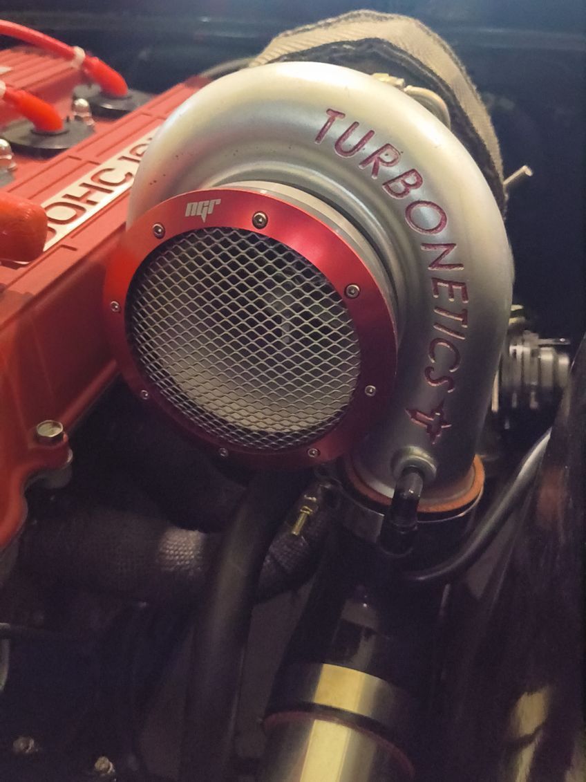 Close-up of a turbocharger with silver piping and a red housing in an engine bay