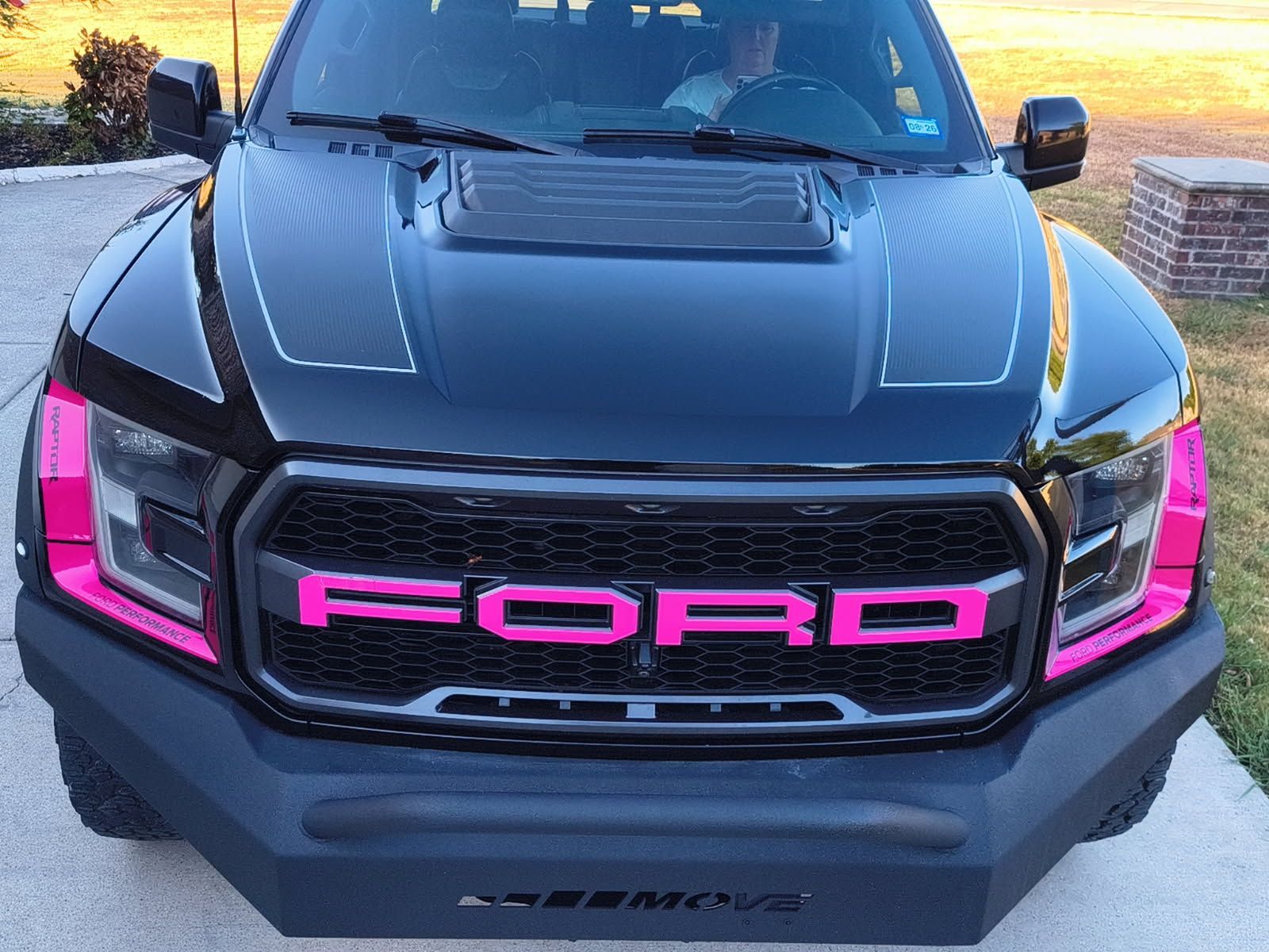 Front view of a black Ford truck with bright pink trim and grille accents parked outdoors at sunset