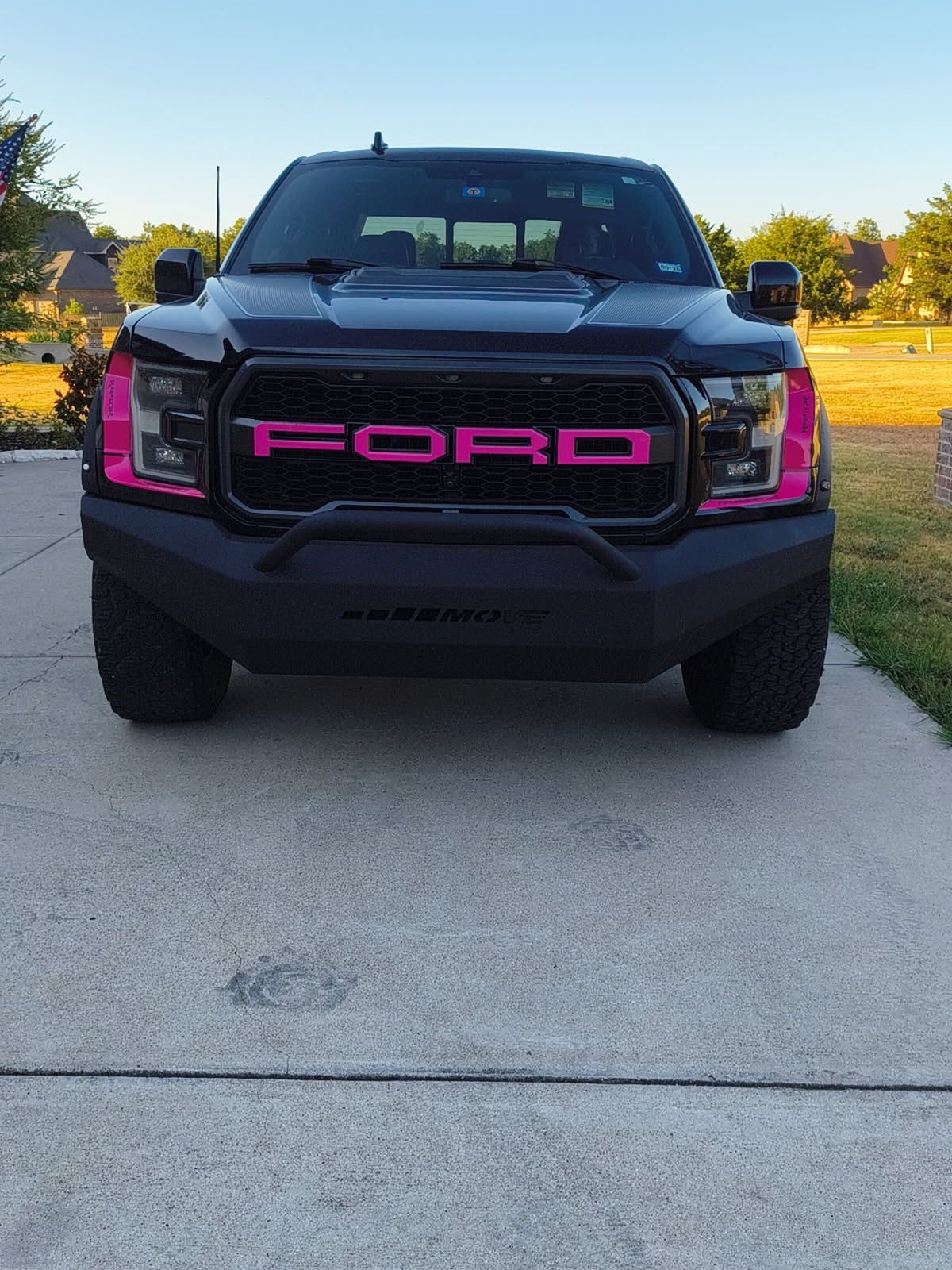 Front view of a black Ford truck with bright pink grille lettering parked on a driveway at sunset