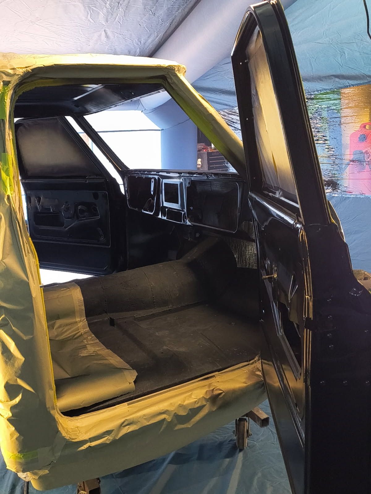 Open car door revealing a black-and-yellow upholstered interior in a garage or workshop.