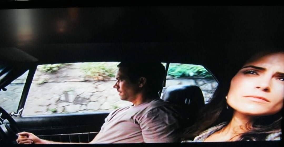 Two people sitting in a car, with a woman in the foreground looking out pensively.