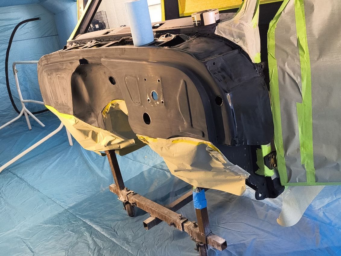 Partially painted car body on a stand in a workshop, masked with tape and plastic sheeting