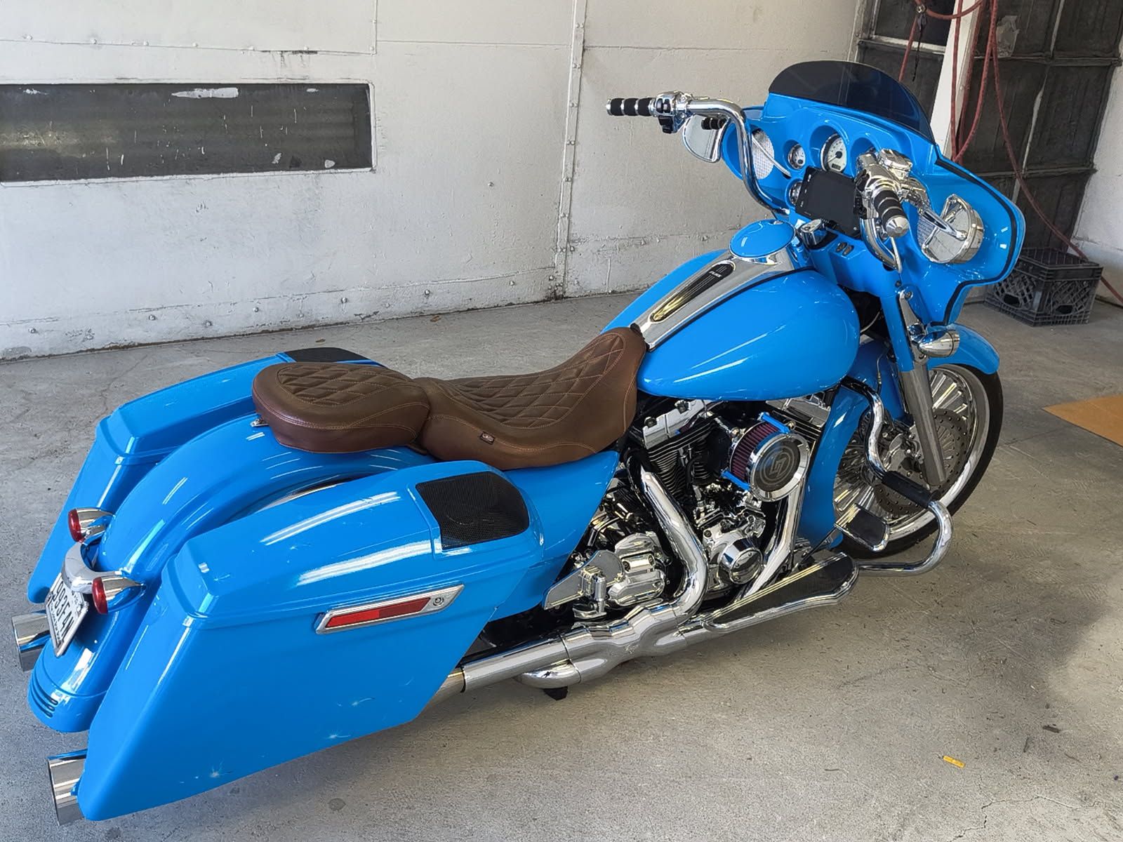 Blue custom motorcycle with brown seat parked indoors on a concrete floor.