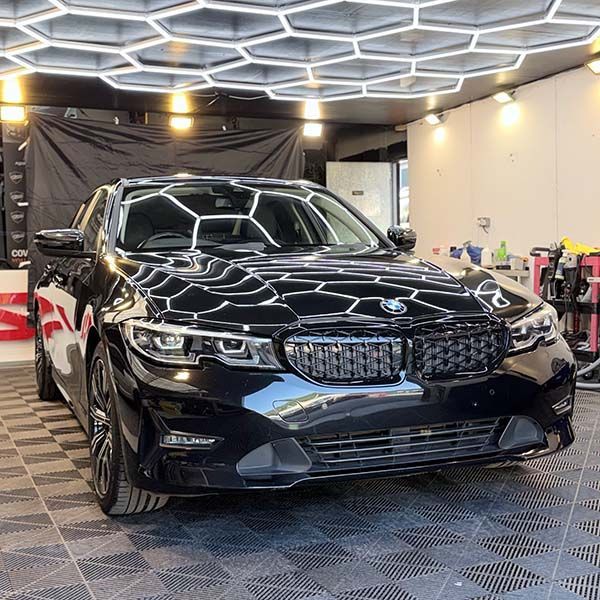 Black BMW sedan in a showroom-like garage with a geometric ceiling and bright overhead lights