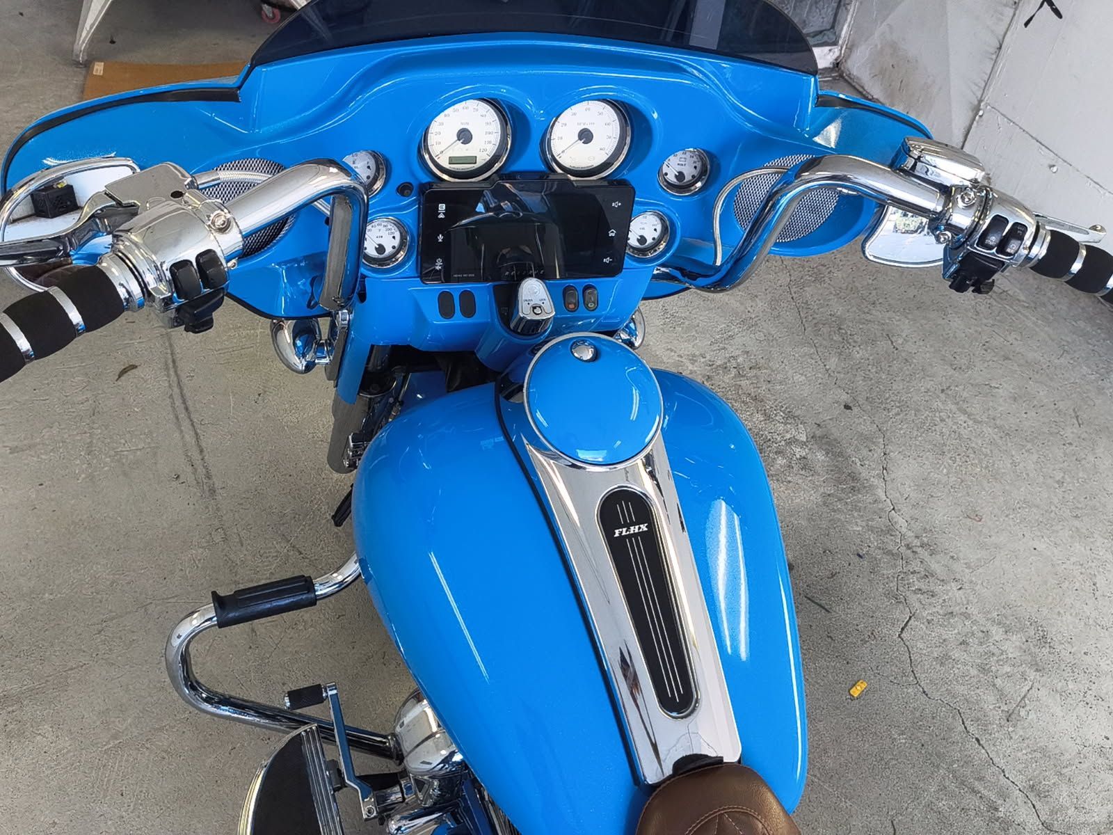 Blue motorcycle handlebars and dashboard viewed from above, parked on concrete.