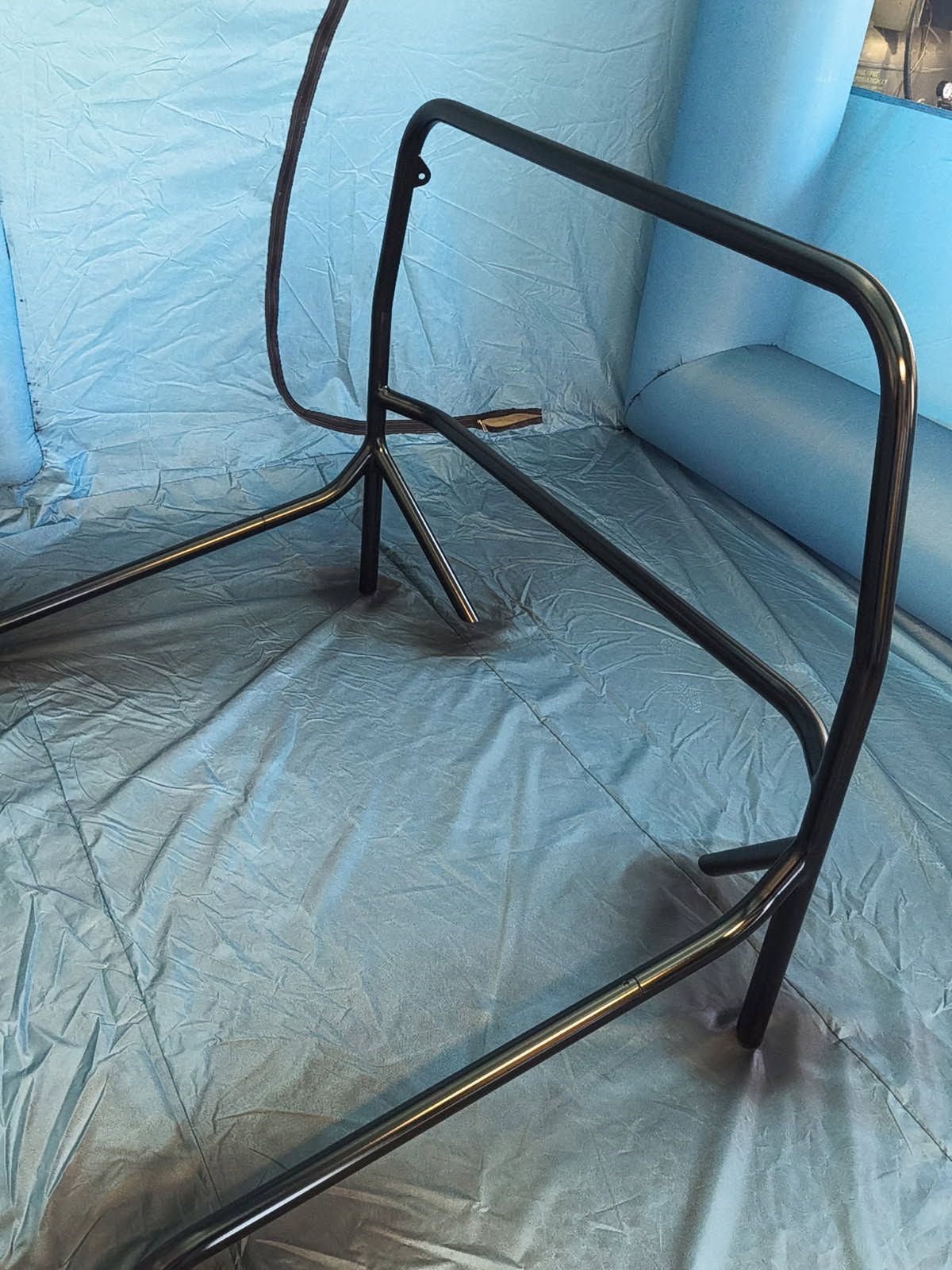 Black metal walker frame on a blue tarp against a blue wall, with a loose cable hanging nearby