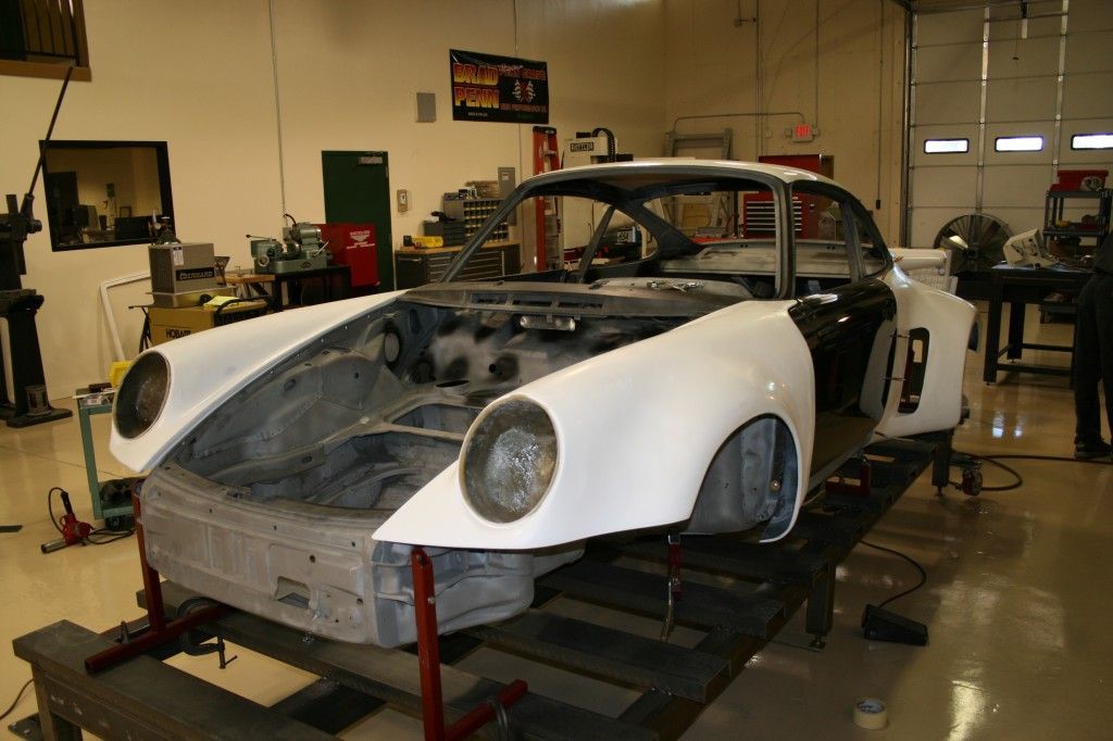 White sports car under repair in a garage, with front body panels removed and wheels on stands.