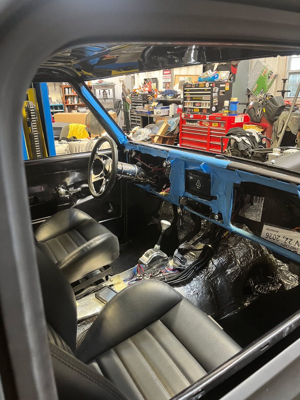 Interior of a blue-and-black custom car in a workshop, with bucket seats, steering wheel, and exposed dash