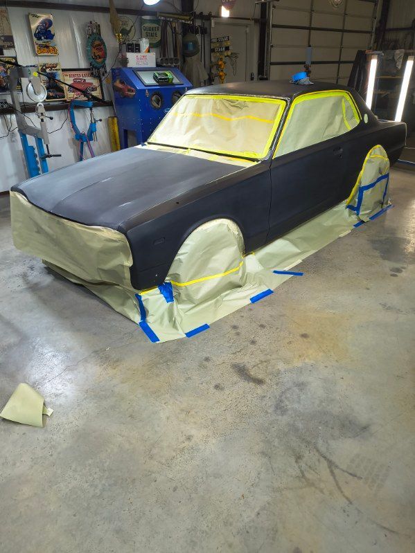 Masked car body in a garage, covered with black and yellow paint-prep tape and paper.