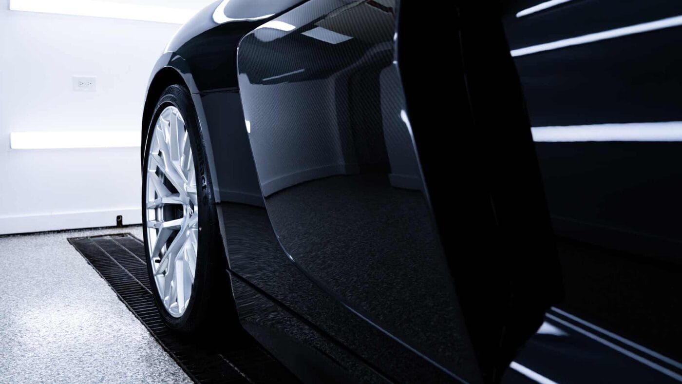 Close-up of a black car’s side and silver wheel in a clean garage or showroom.