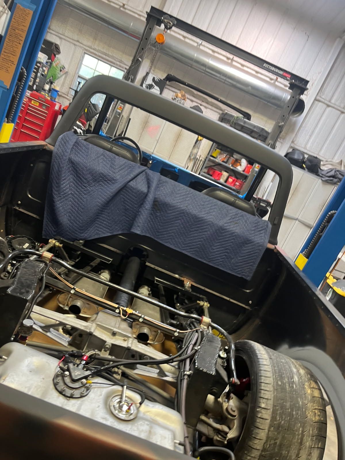 Partially stripped car in an auto shop, with exposed engine and rear wheel visible.
