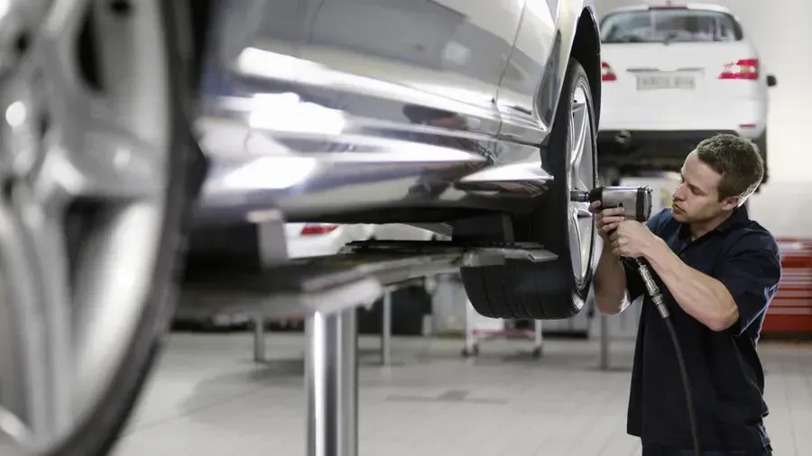 Mechanic inspecting the underside of a silver car in an auto repair shop