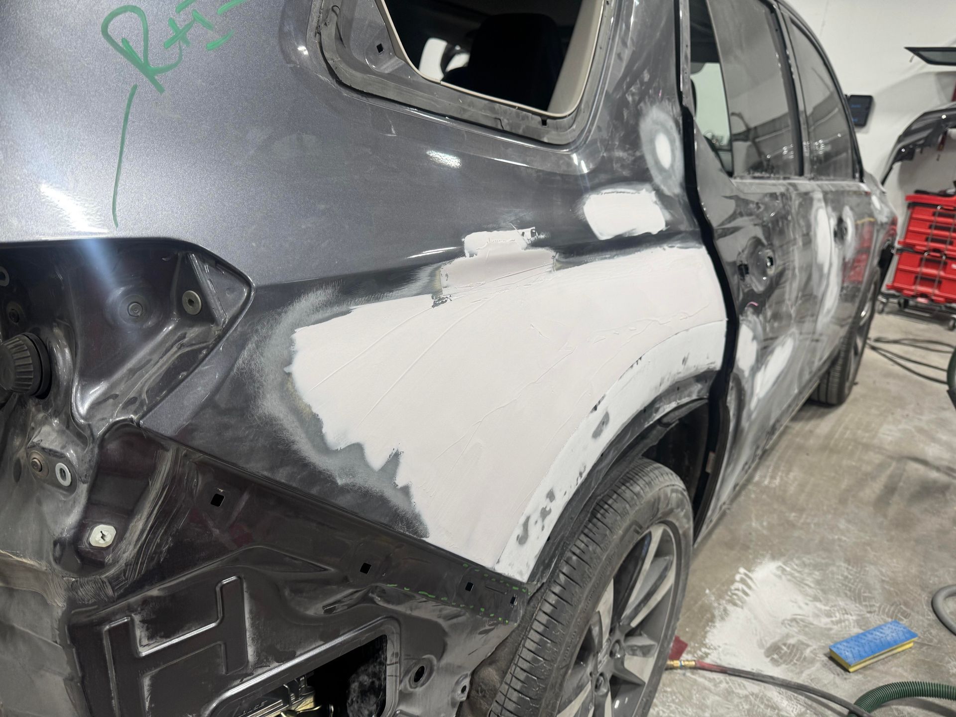 Damaged black SUV with gray primer on the rear quarter panel in an auto body shop