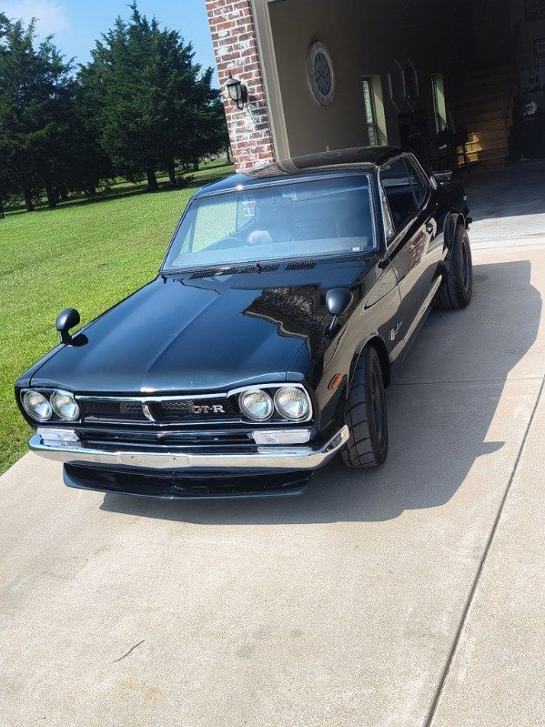 Black classic car parked on a driveway beside a brick house in bright sunlight