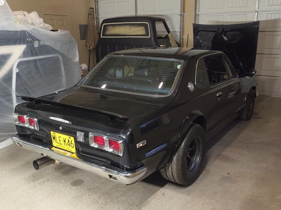 Black classic car parked in a garage, viewed from the rear with a yellow license plate.