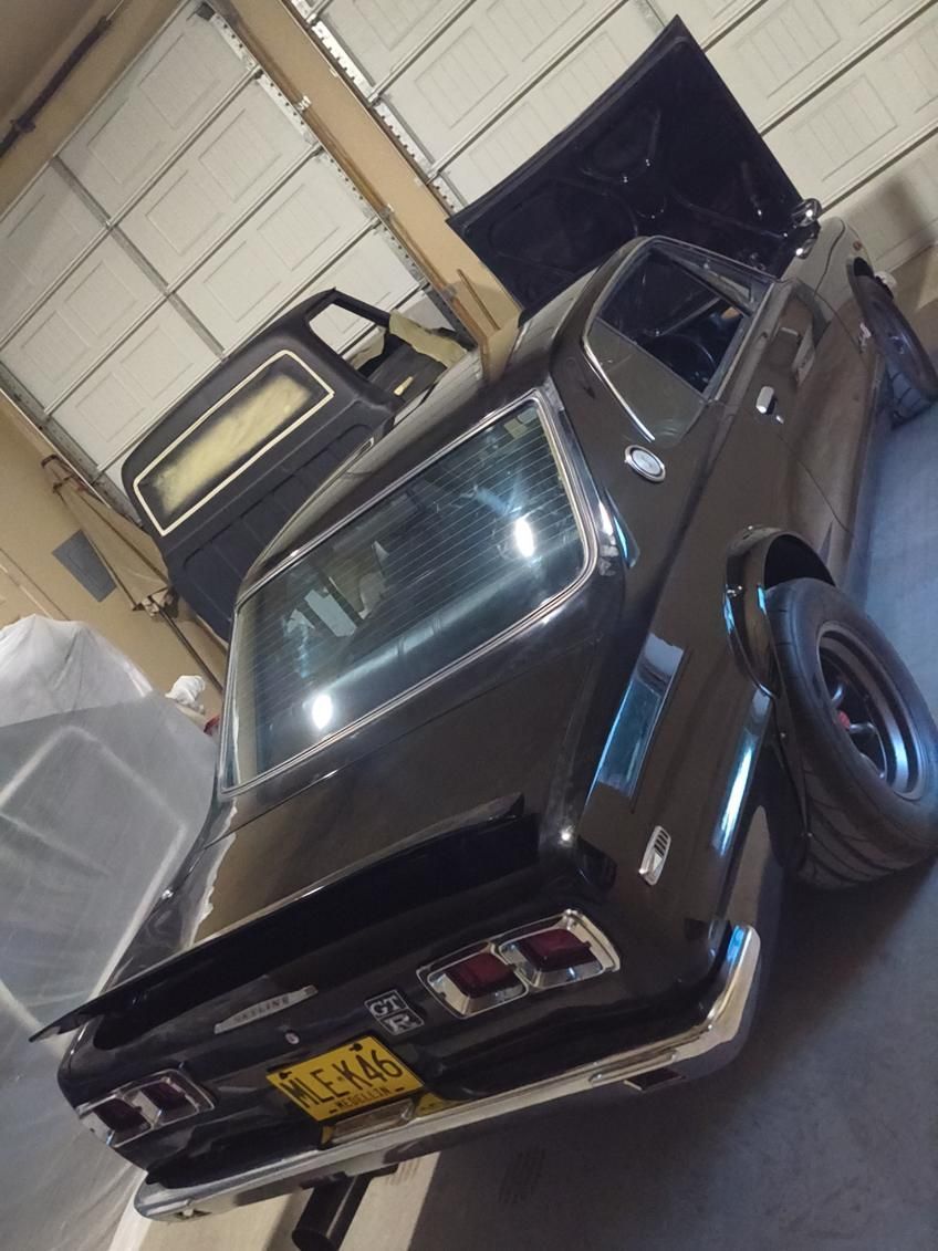 Black classic car parked inside a garage, viewed from the rear three-quarter angle.